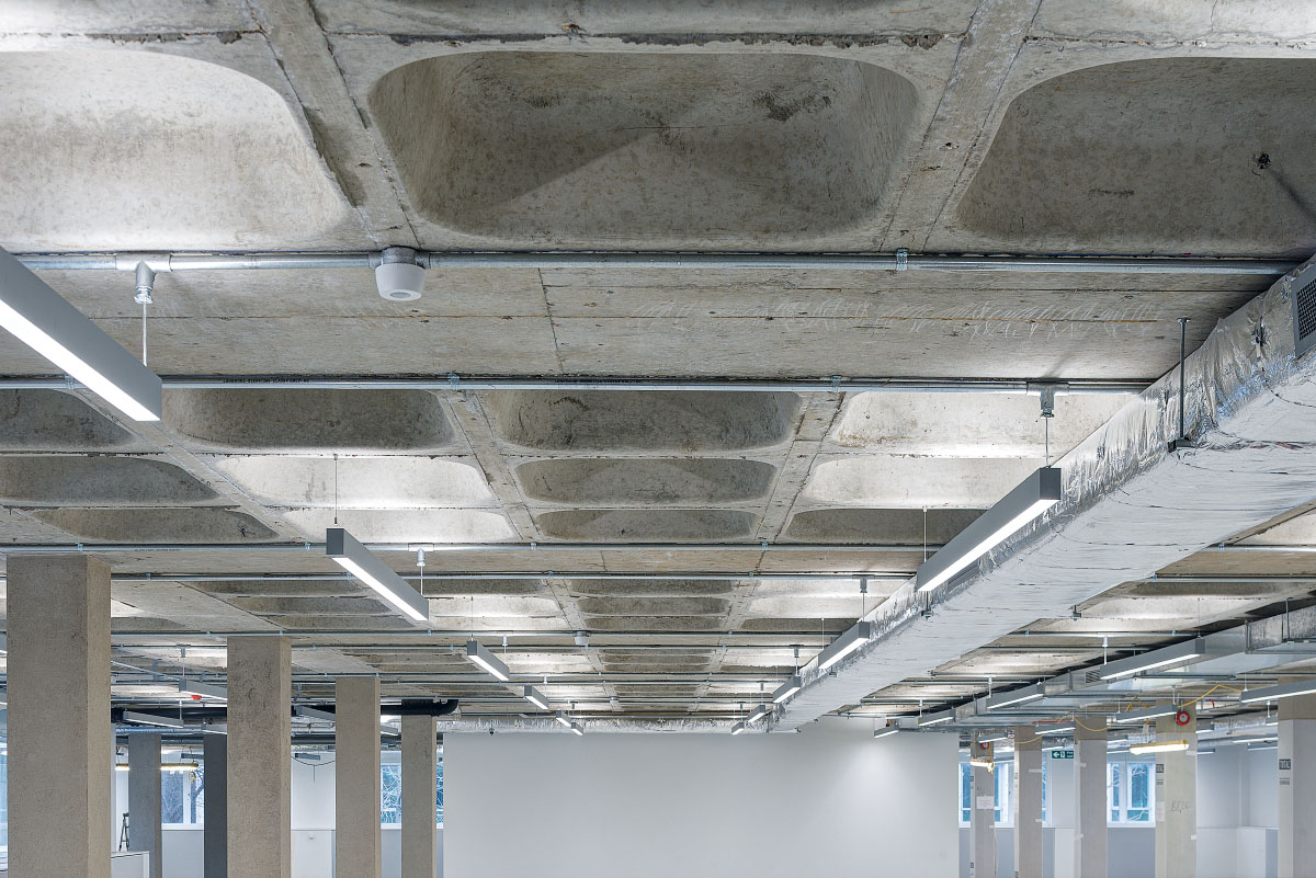 Detailed view of the industrial ceiling at Glen House, showcasing exposed concrete with recessed sections, suspended linear lighting, and visible ductwork.