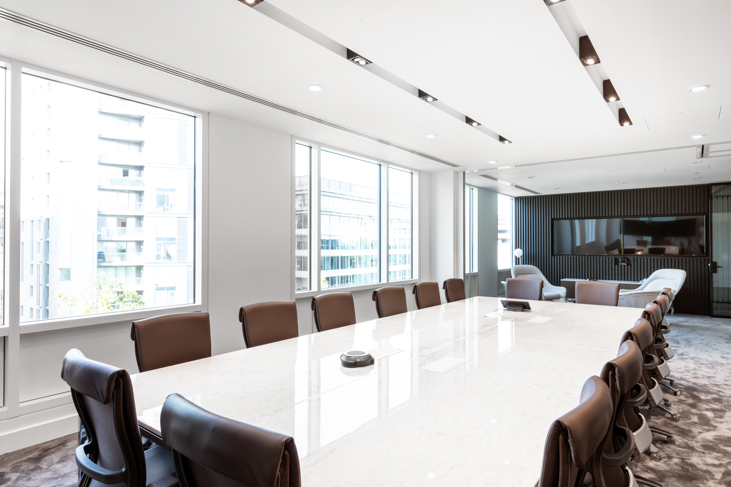 A comfortable lounge area in the Ring Central office, equipped with stylish black chairs, a wall-mounted screen, and textured black panelling, creating a relaxed yet professional setting.