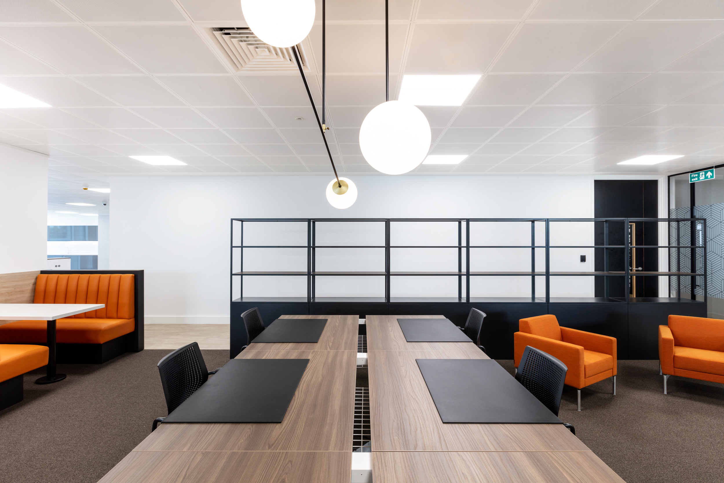 A collaborative workspace at Ring Central with wooden tables, orange seating, and pendant lighting. The space encourages productivity and creativity.