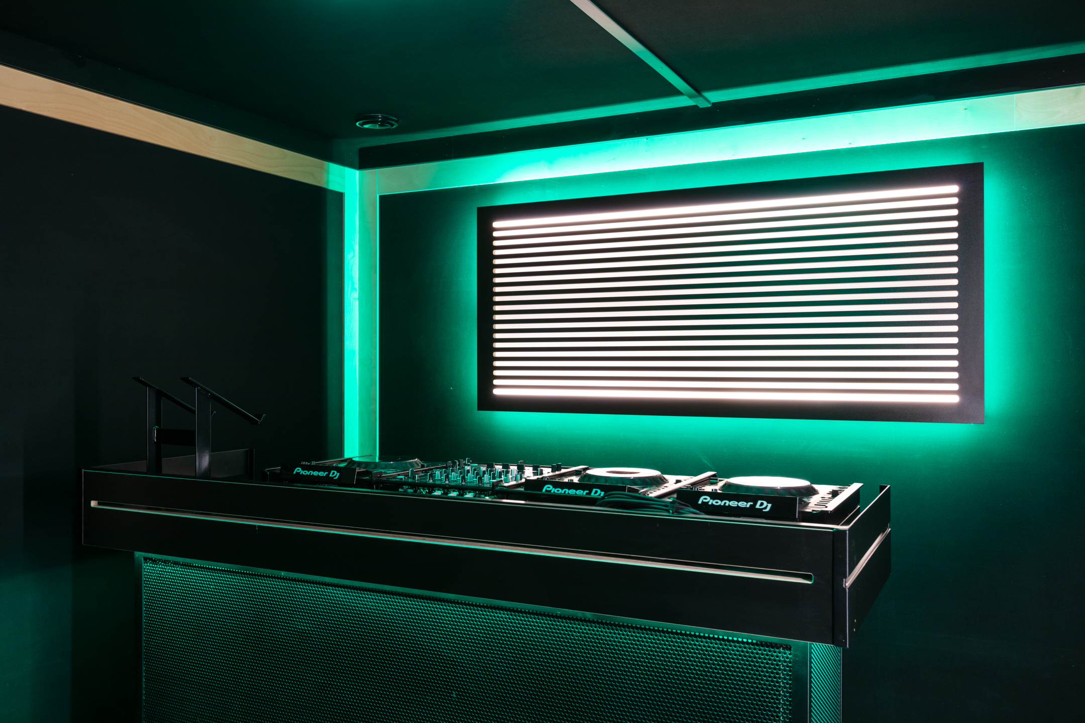 A the DJ booth at Pirate Studio, this time with green lighting around the illuminated backdrop, adding a vibrant atmosphere to the dark room.