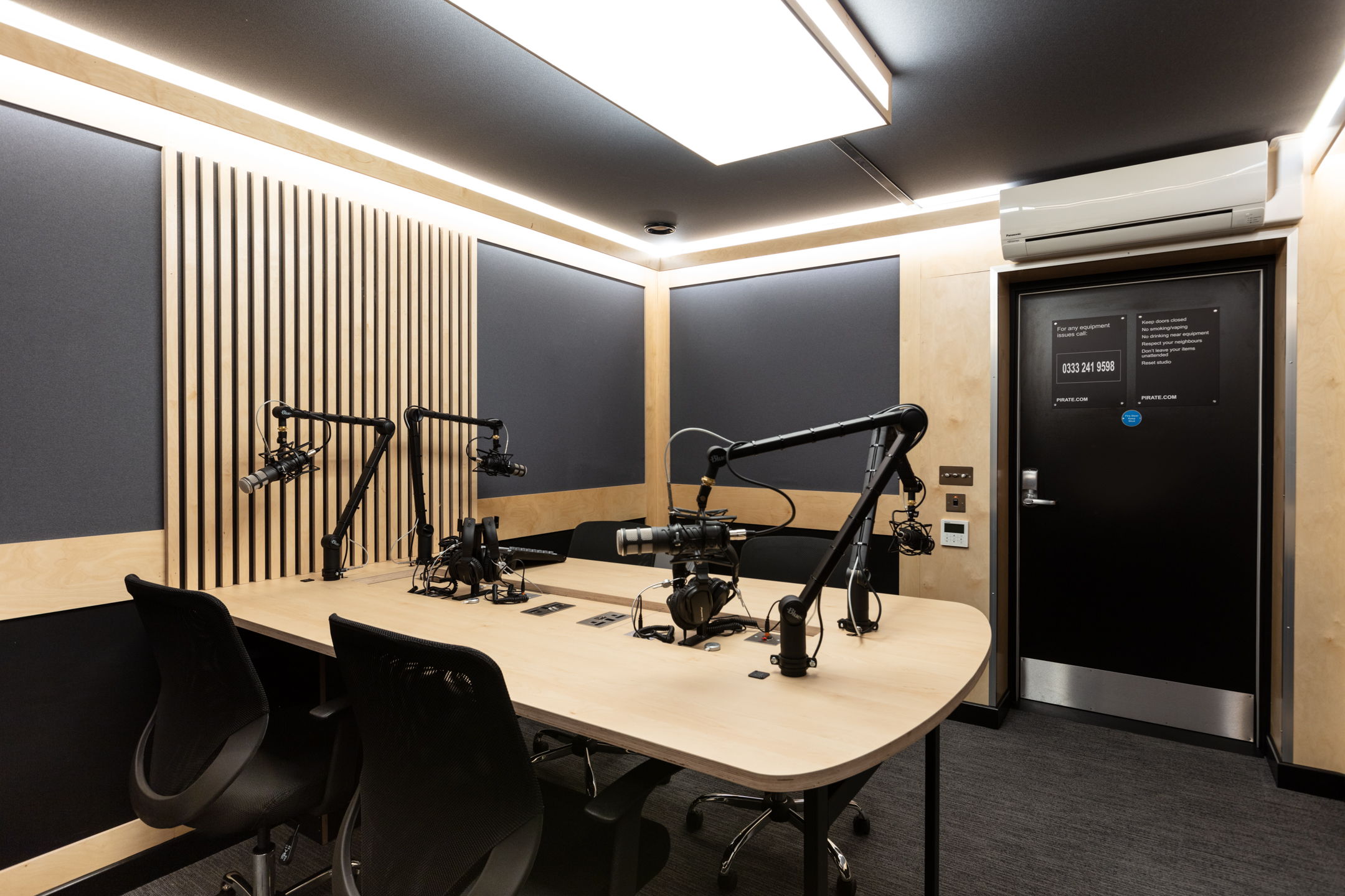 A podcast recording studio at Pirate Studio, equipped with professional microphones, a mixing console, a wooden table, and soundproofed walls for high-quality audio recordings.