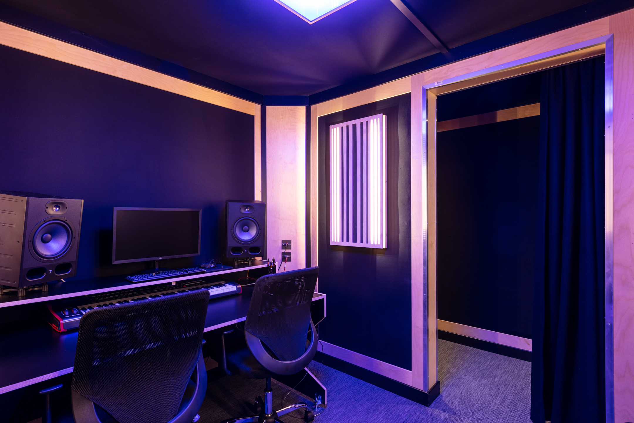 A music production room at Pirate Studio, featuring a setup with a keyboard, monitor, two studio monitors, and LED lighting in a soundproofed environment.