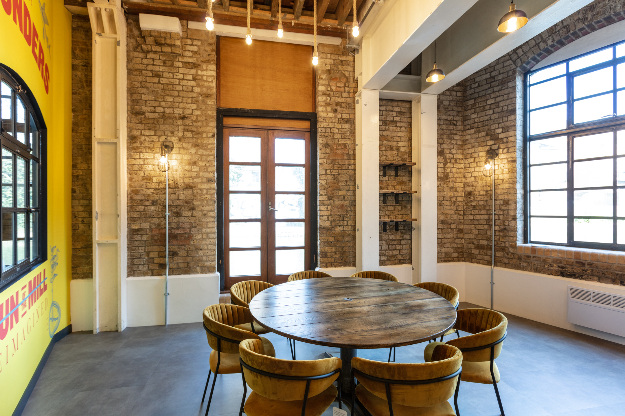 Round Table Meeting Area at Regent's Wharf: A round table surrounded by velvet chairs in a meeting area at Regent's Wharf, showcasing exposed brick walls and industrial lighting.