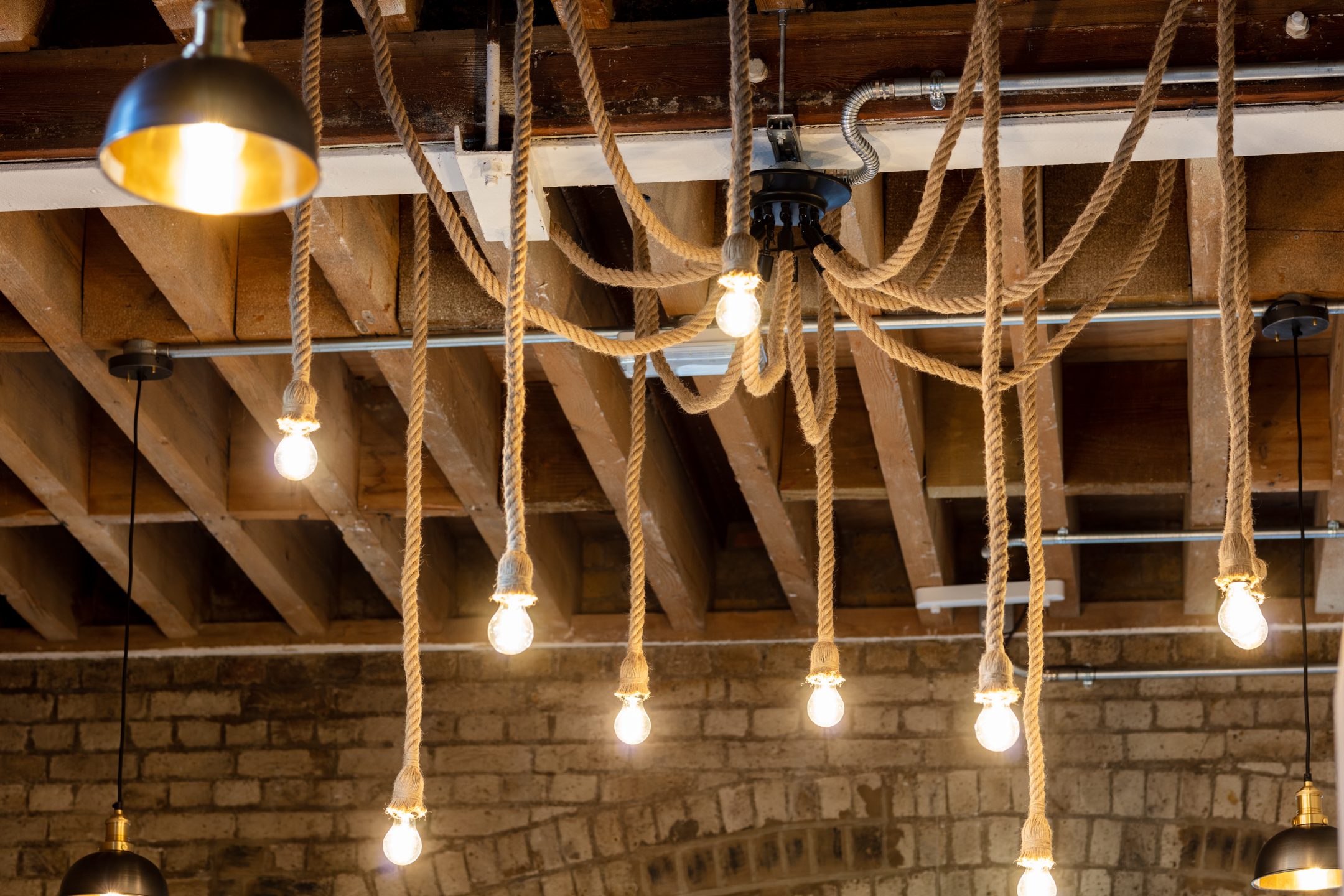 Rustic Lighting Design at Regent's Wharf: Close-up of the rustic lighting design at Regent's Wharf, featuring rope-wrapped pendant bulbs hanging from the ceiling, complementing the industrial aesthetic