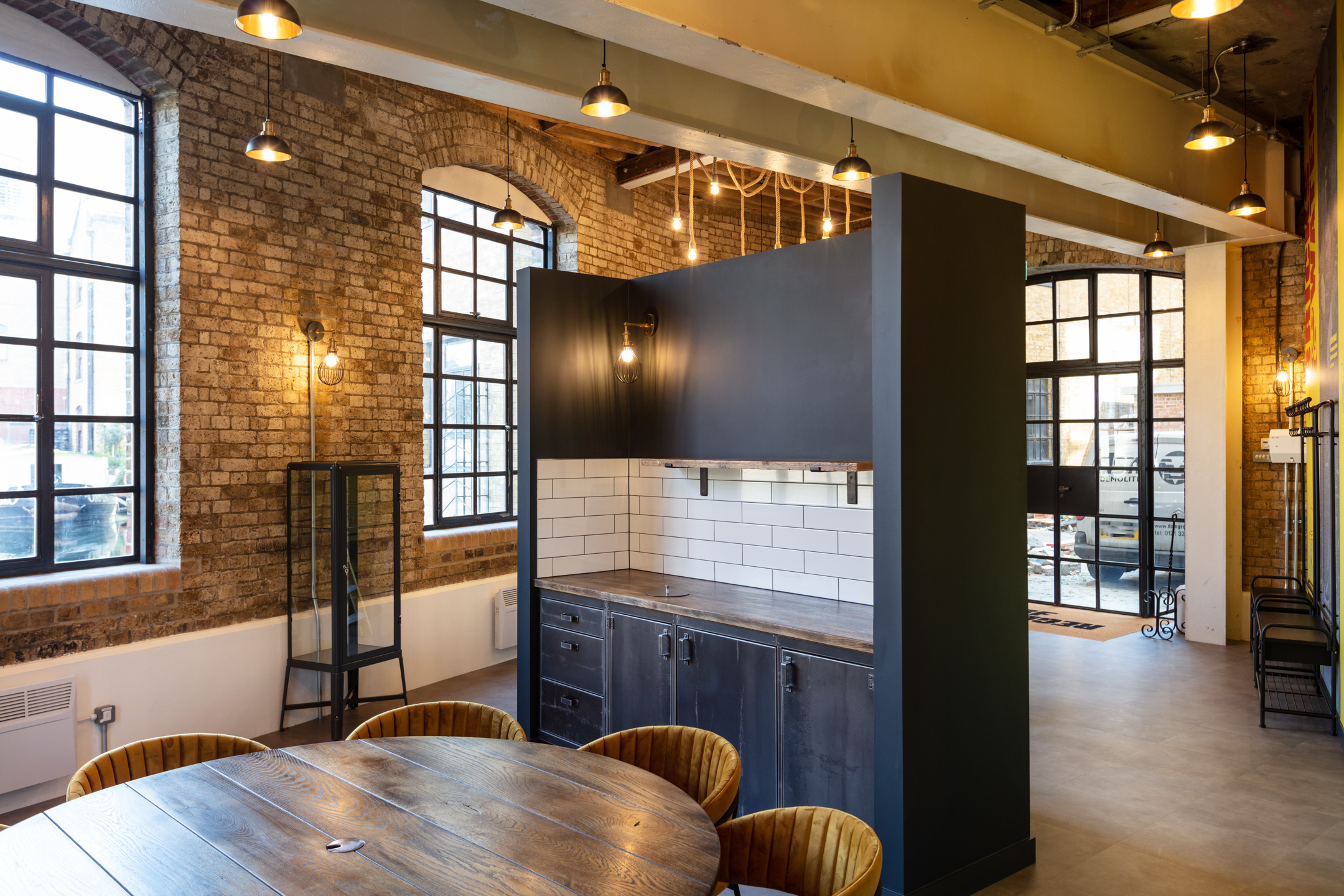 View of Teapoint and Windows at Regent's Wharf: A view of the kitchenette and large windows at Regent's Wharf, with exposed brick walls and pendant lighting, offering a blend of industrial and modern design elements.