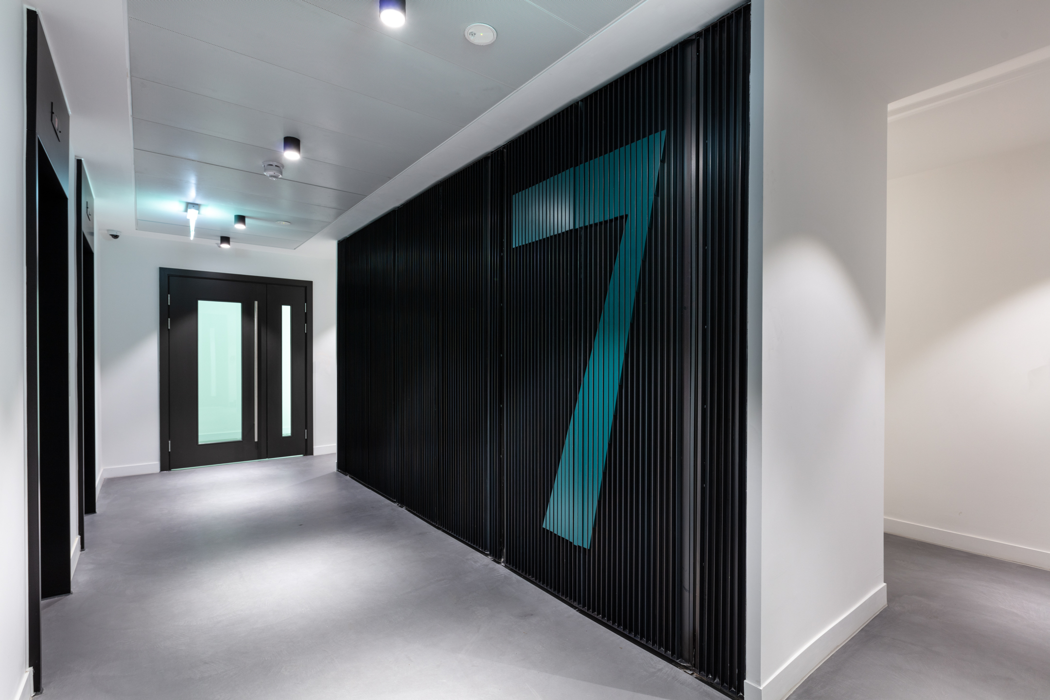 A hallway at Programme Building, featuring sleek black walls and a large teal number 