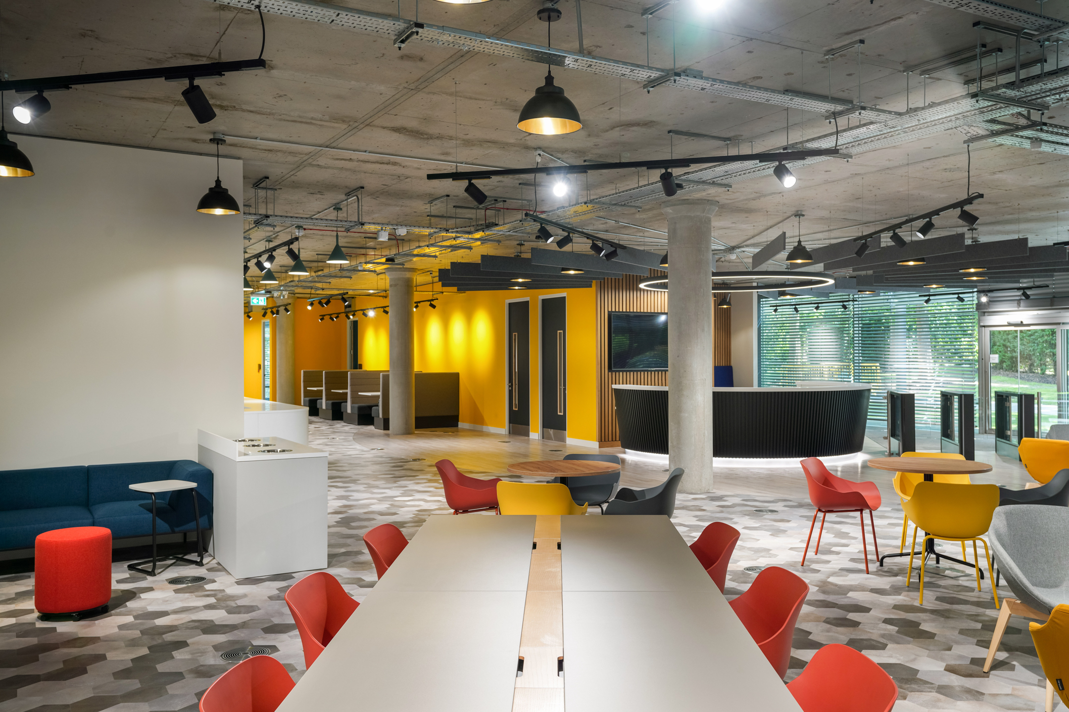 Dynamic social and collaborative space at Richmond University with colourful chairs, modular seating, vibrant yellow accent walls, and an industrial ceiling design, creating a welcoming environment.