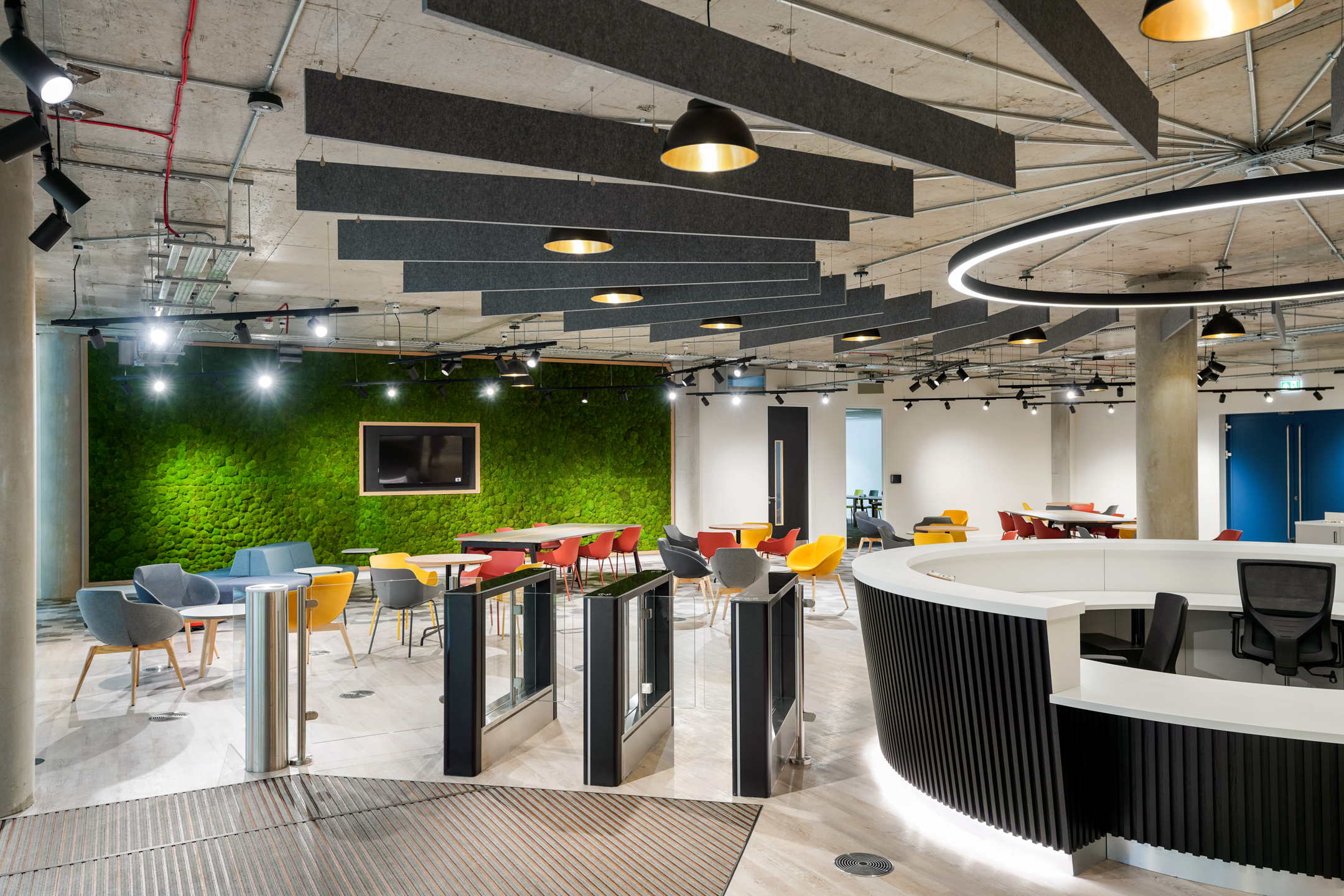 Contemporary lobby area at Richmond University with a circular reception desk, moss feature wall, colourful seating, acoustic ceiling baffles, and glass entry gates.