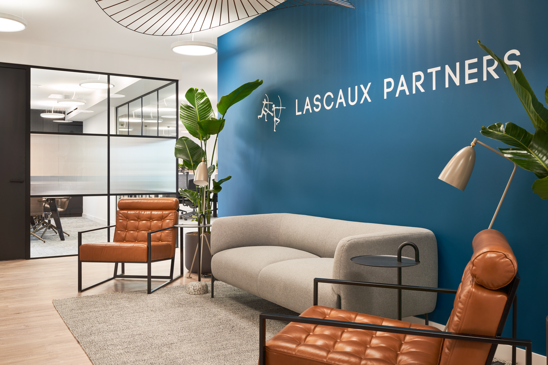 Reception area at 3 St Helens Place for Lascaux Partners, featuring a bold blue accent wall, comfortable leather armchairs, a modern grey sofa, and indoor plants for a welcoming atmosphere.