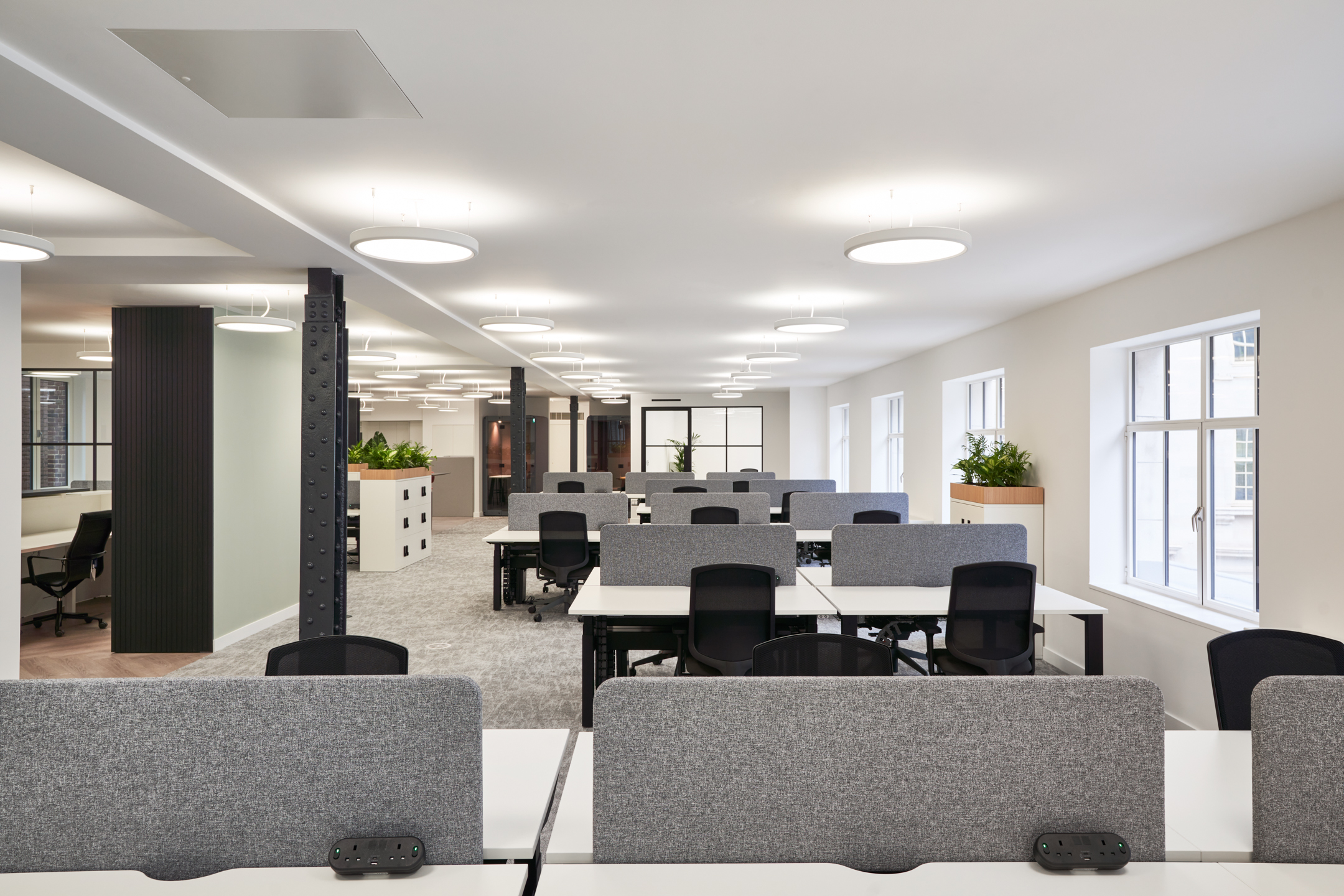 Open-plan workspace at 3 St Helens Place featuring rows of desks with grey privacy screens, ample natural light from large windows, and integrated storage with greenery for a functional and refreshing office setting.