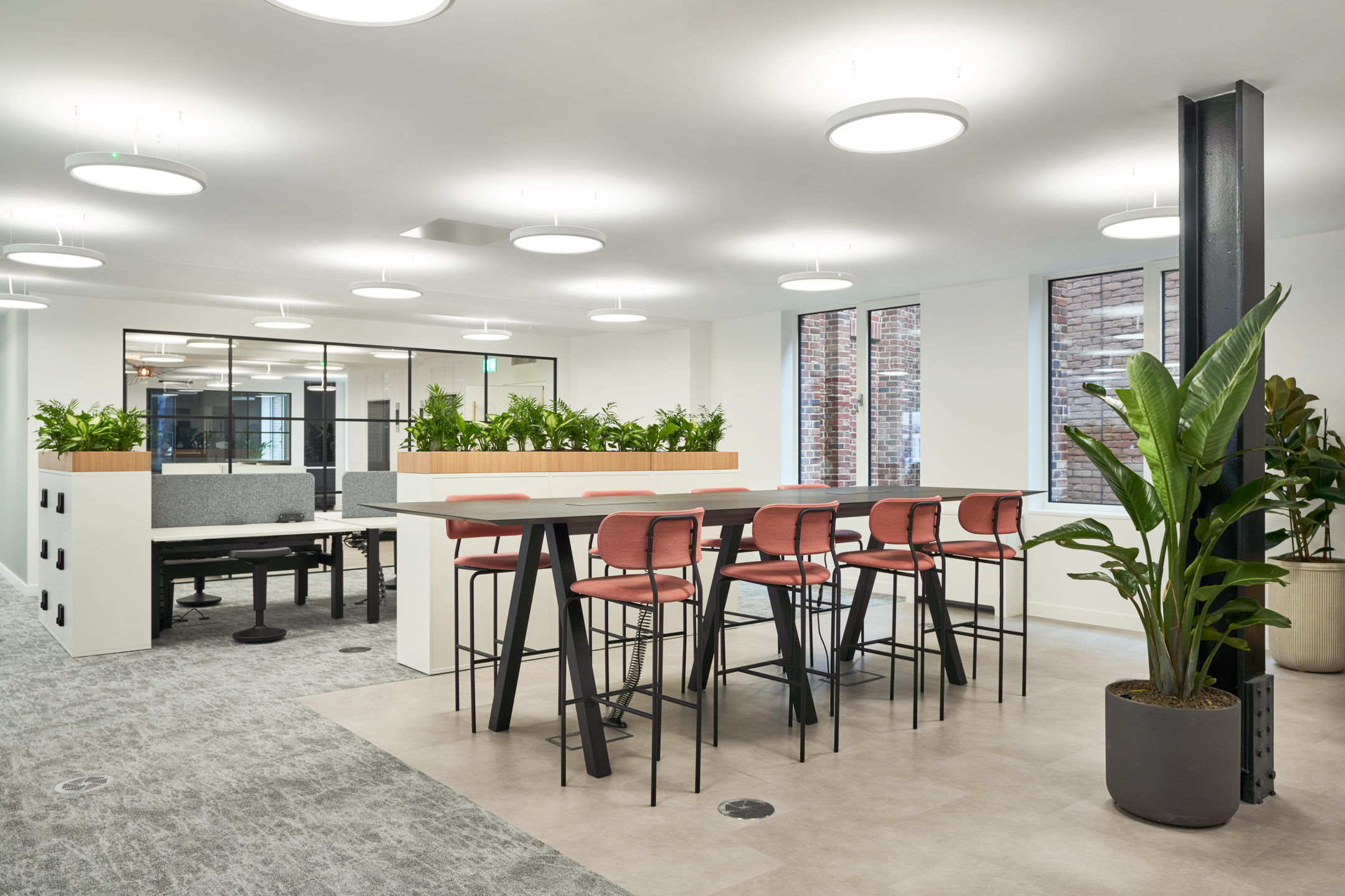 Collaborative area at 3 St Helens Place with a high table and red bar stools, surrounded by greenery-filled storage units.