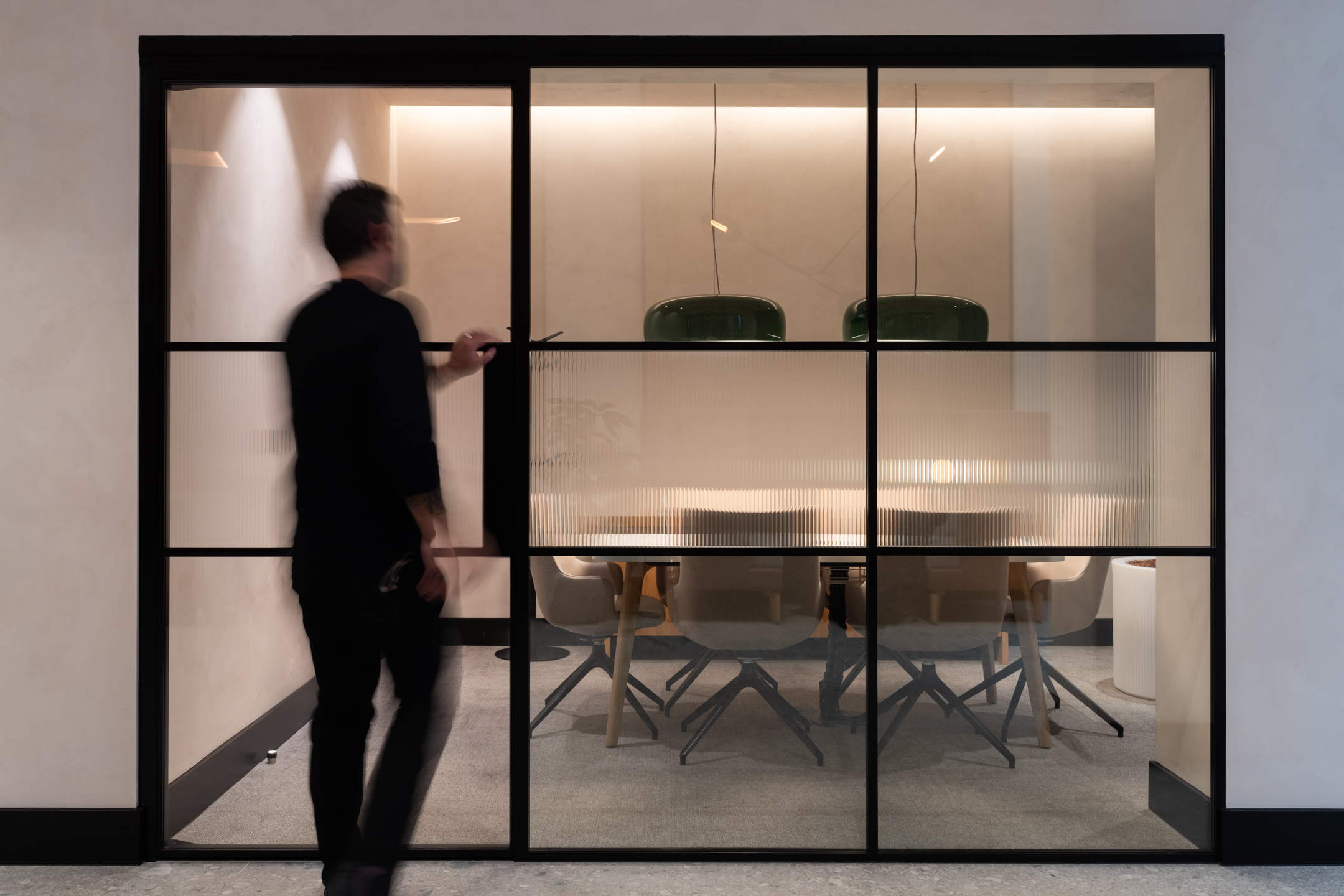 A view through a partially frosted glass door leading to a private meeting room. A person is visible, opening the door, with a glimpse of the meeting room's furnishings inside.