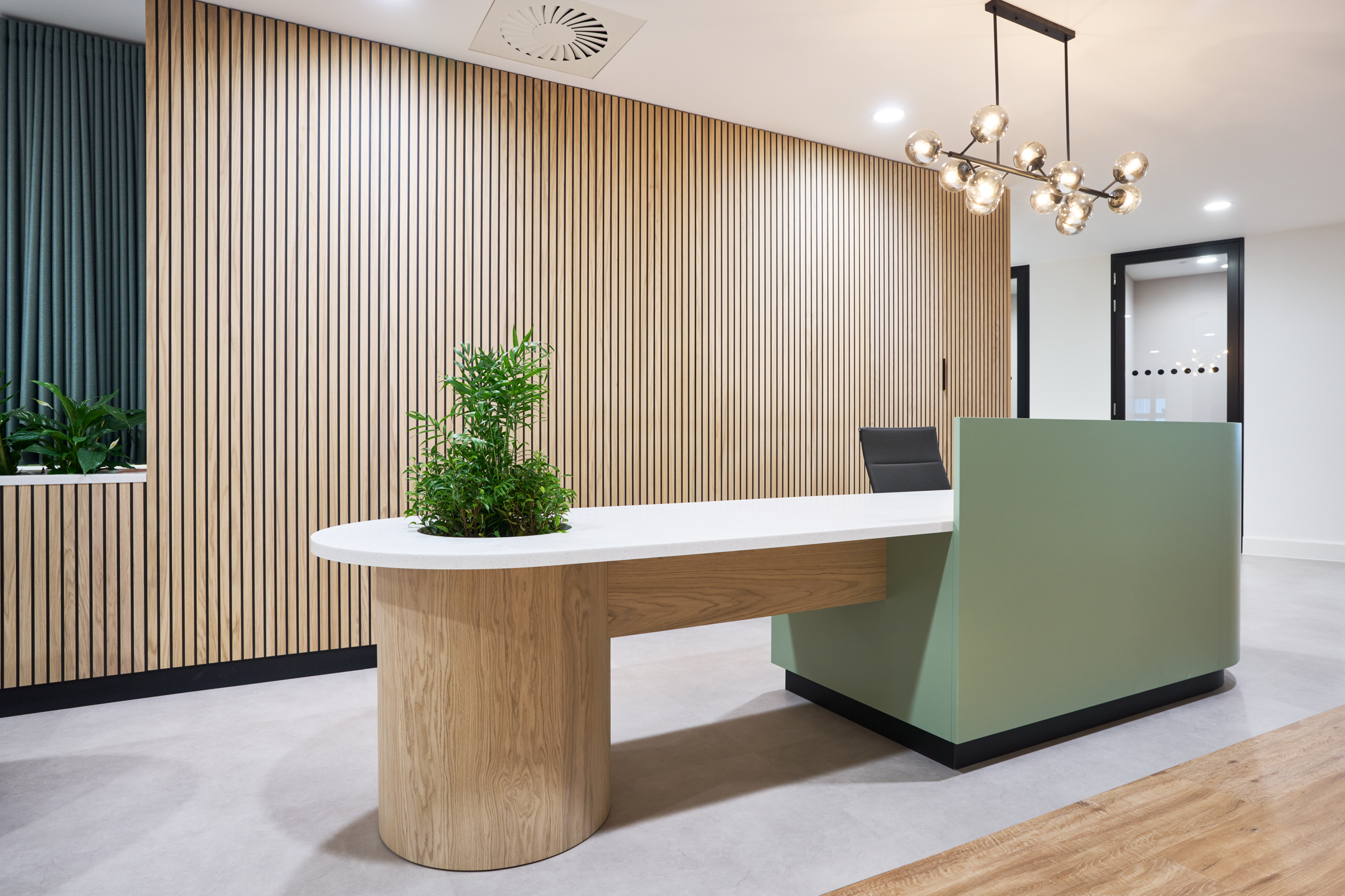 Reception desk at 7 Bishopsgate Level 4, featuring a curved design with wood and green accents, and a modern chandelier overhead.