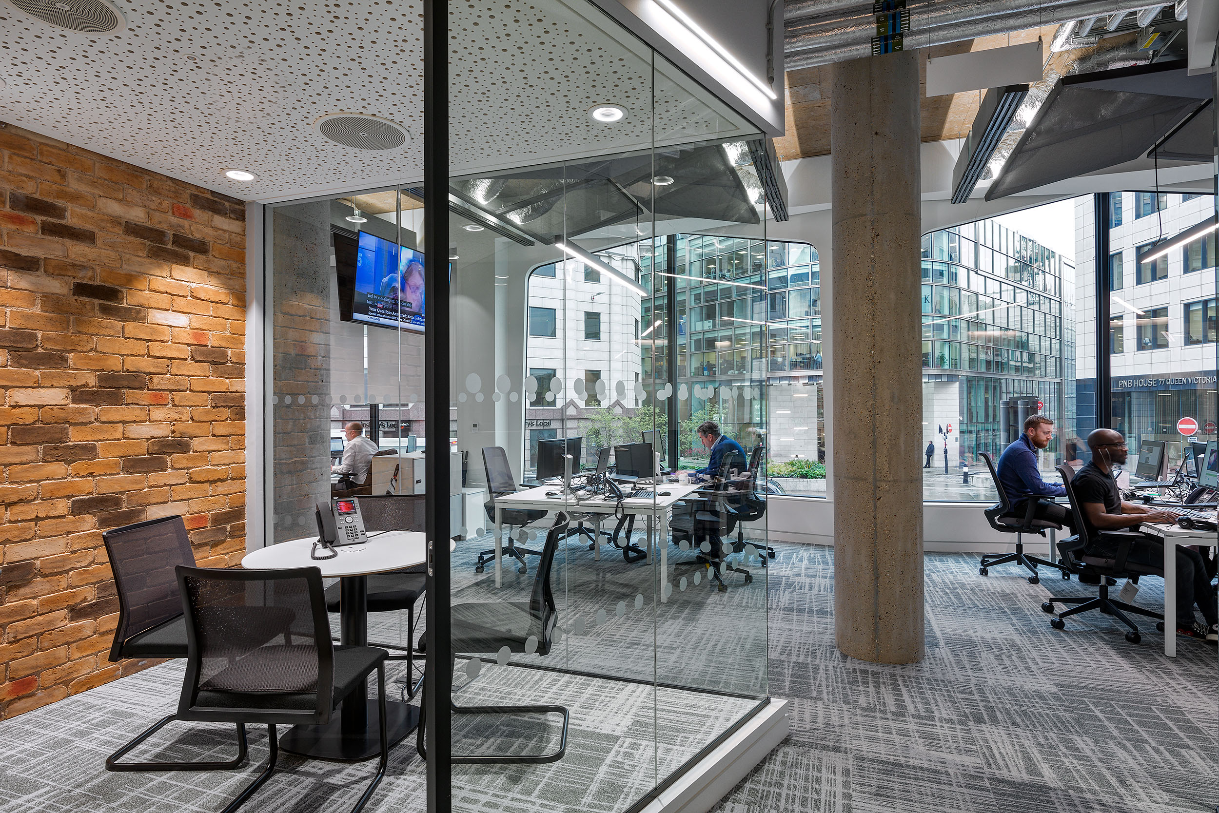 Asset TV’s open-plan office space featuring glass-walled meeting rooms, modern furniture, and floor-to-ceiling windows allowing natural light. The space is divided into various workstations.