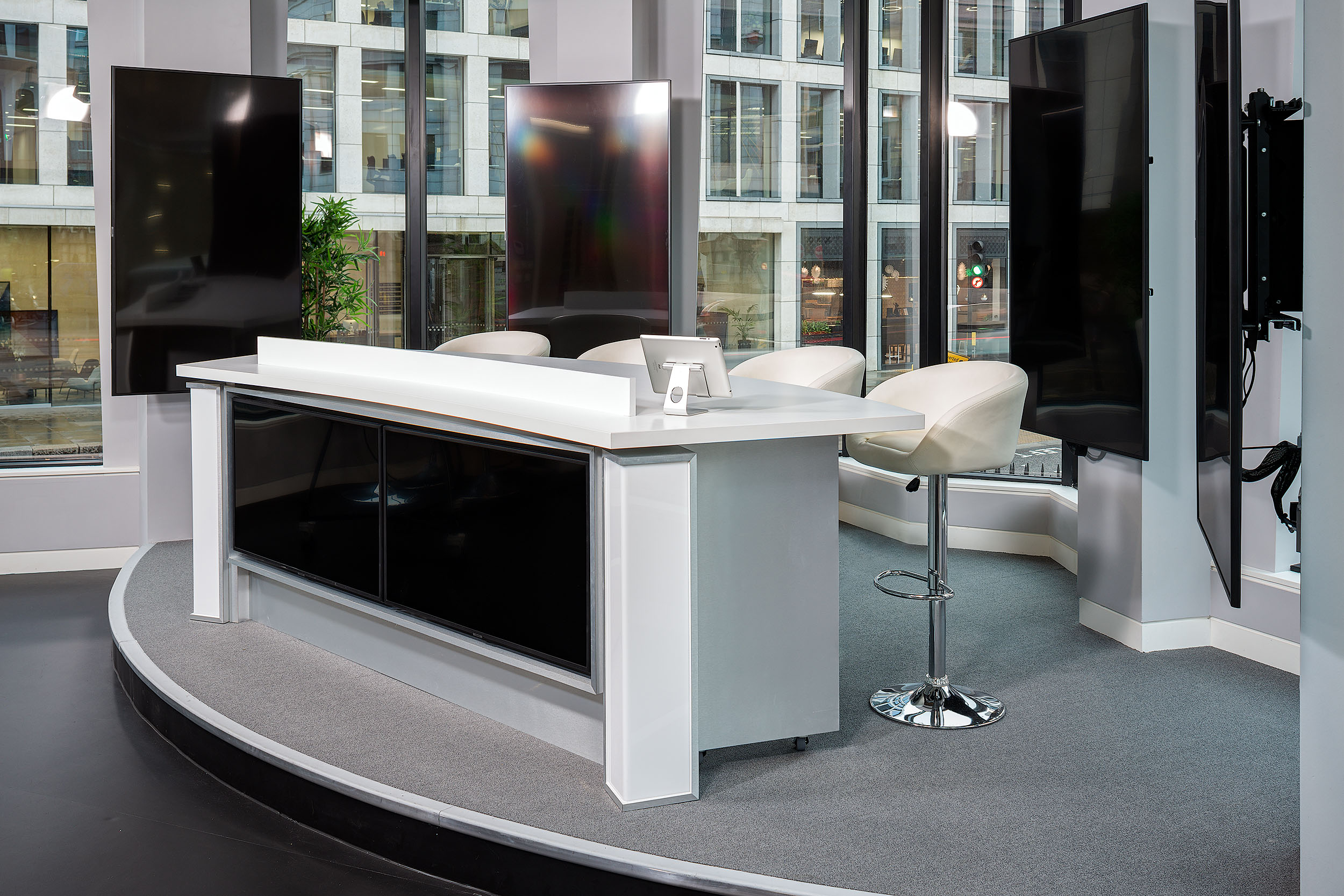 A close-up of the studio desk at Asset TV, surrounded by multiple screens. The studio setup includes comfortable chairs and a sleek, curved design, creating a professional on-air environment