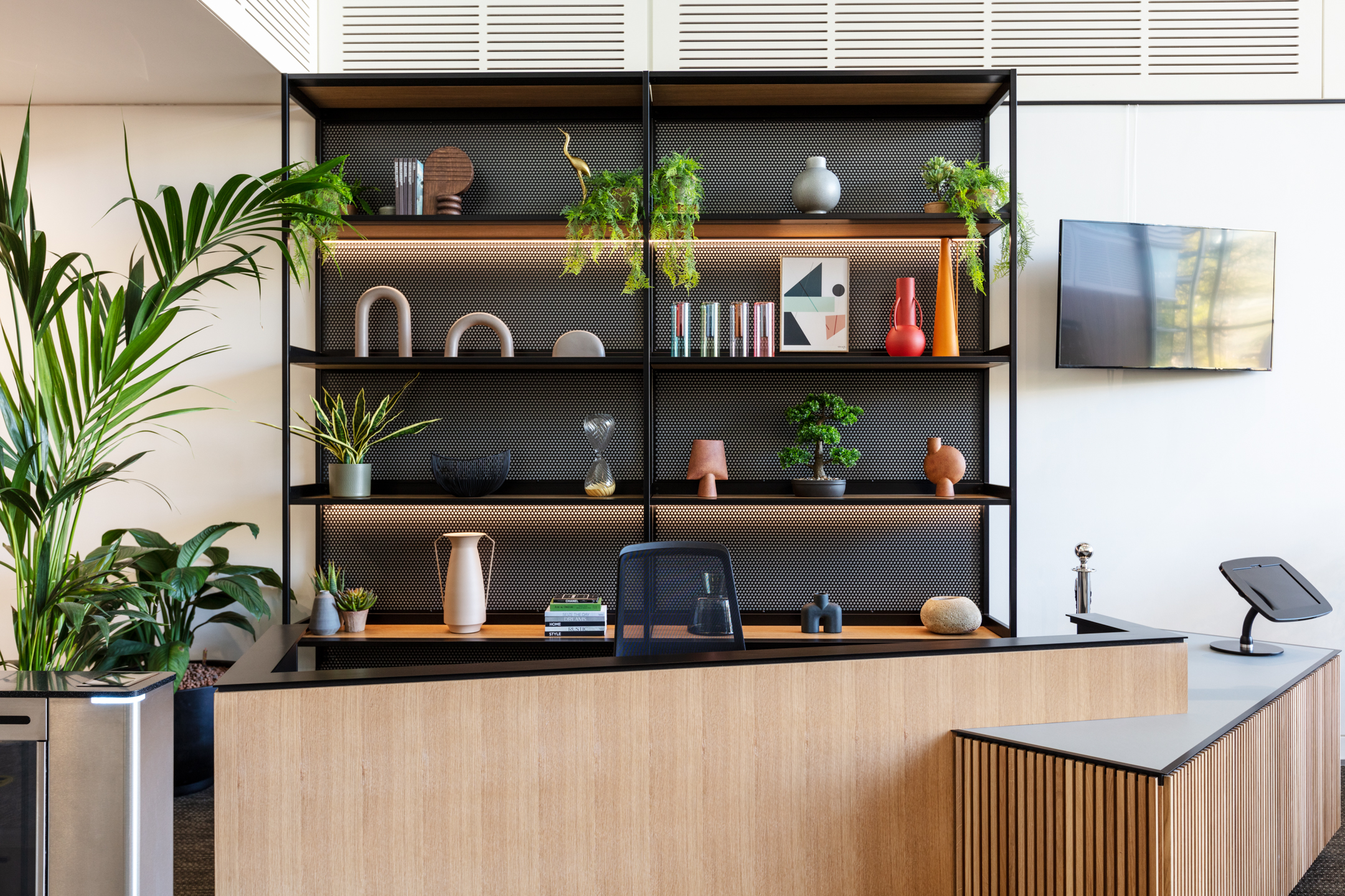 A modern, wood-panelled reception desk with decorative shelves behind, showcasing various plants and decorative accents in Chiswick Business Park Building 9.