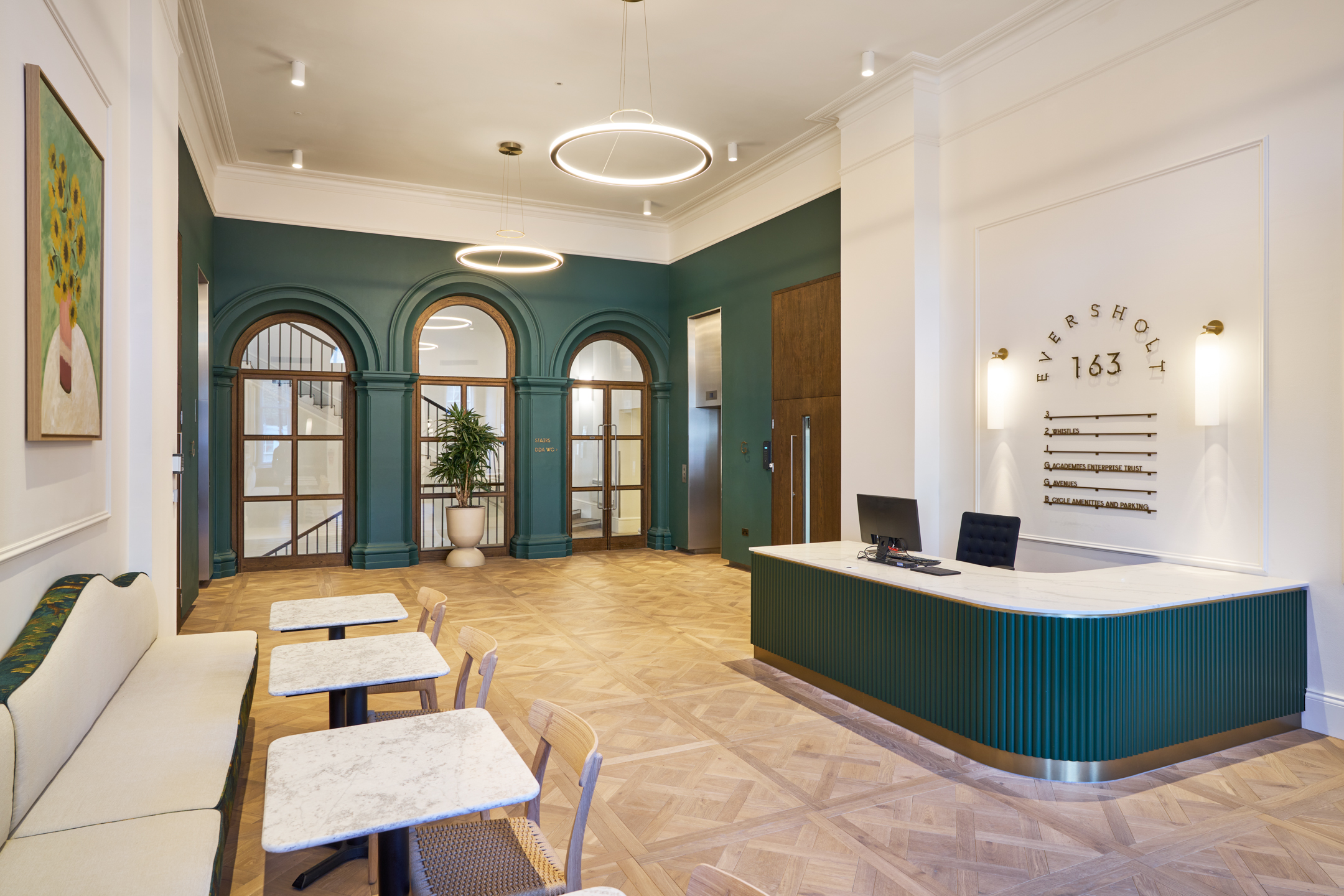 Reception area at 163-203 Eversholt Street, featuring a green accent wall, marble desk, and arched windows, with modern circular pendant lighting.