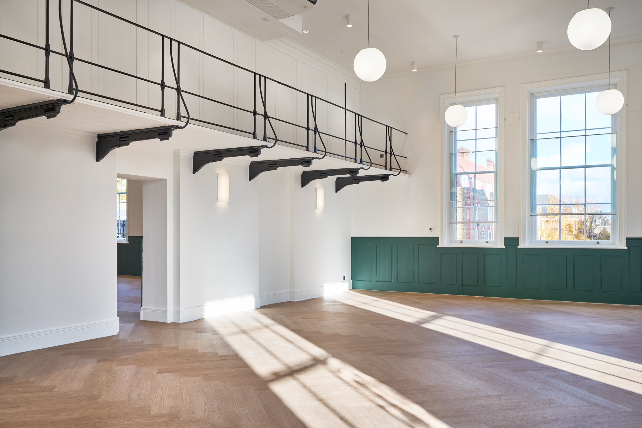 Bright, open room at 163-203 Eversholt Street, with large windows, green panelling, and an upper-level walkway with black railings.