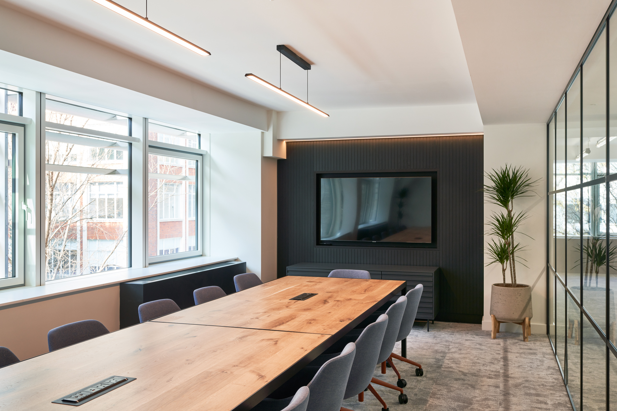 Meeting room at 101 New Cavendish Street, L2, with a large wooden table, grey chairs, and a wall-mounted TV, flooded with natural light.