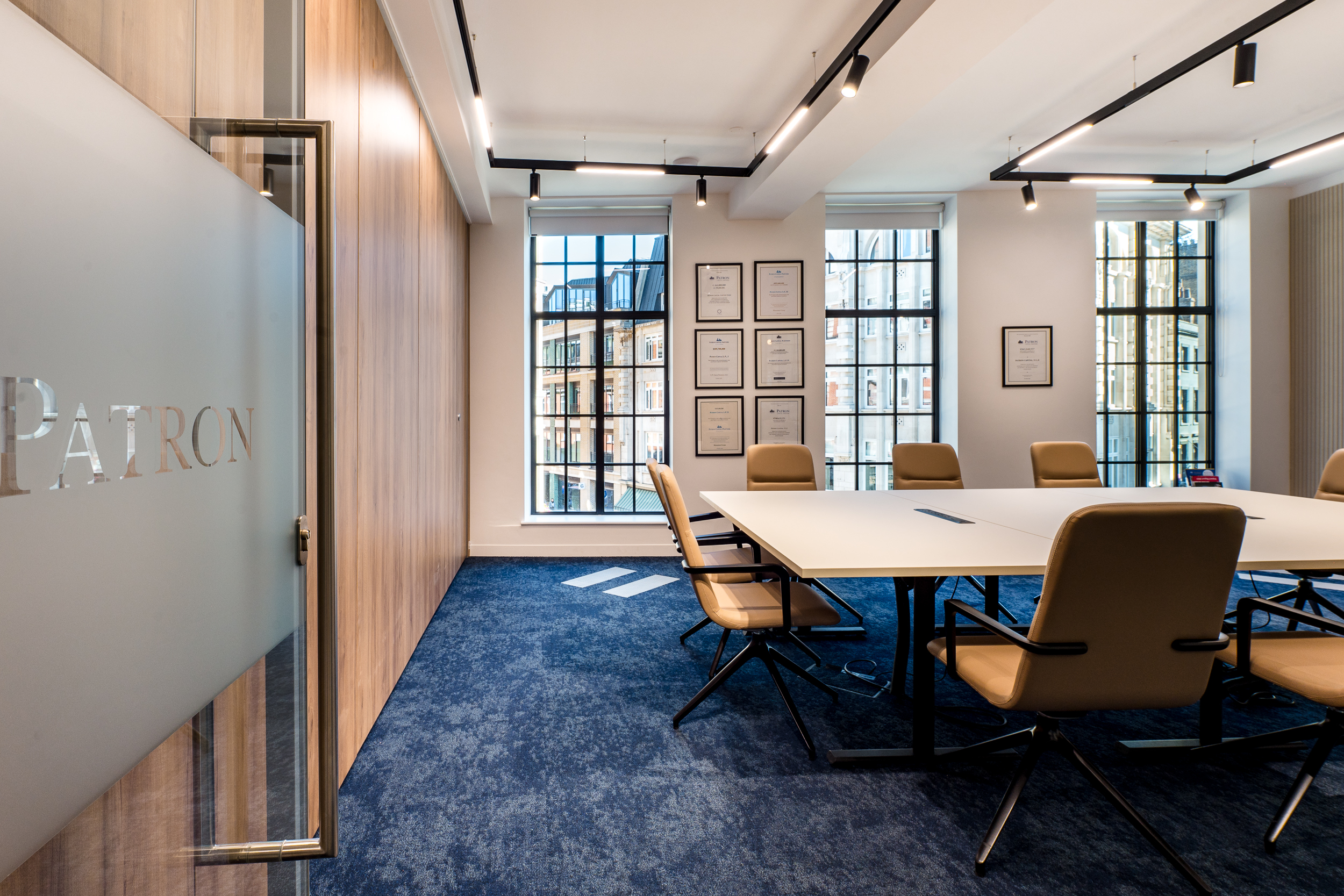 Bright, modern meeting room at Patron with a table and chairs, featuring floor-to-ceiling windows allowing natural light to flood in.