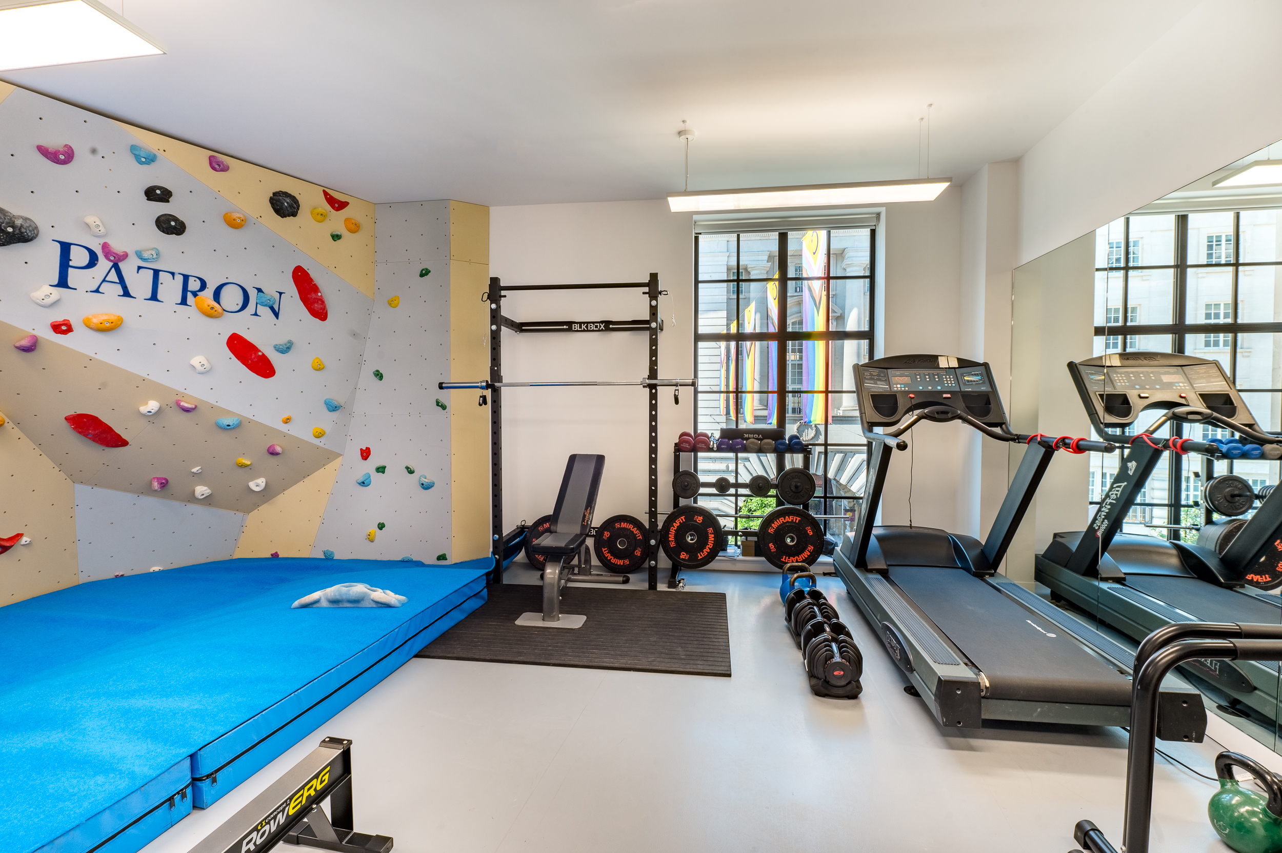 Small gym area with workout equipment and a climbing wall branded with the Patron logo.