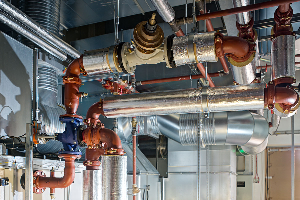 Close-up of industrial piping at Smiths Detection, displaying insulated valves and complex network of red and silver pipes essential for efficient control and flow management within the facility.