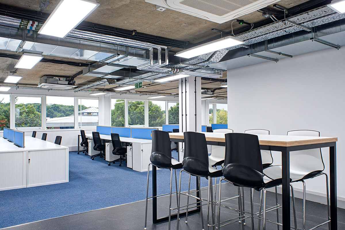 Modern office space at Smiths Detection, featuring an open-plan layout with collaborative seating, ergonomic workstations, and exposed ceiling design, providing a functional and contemporary work environment.