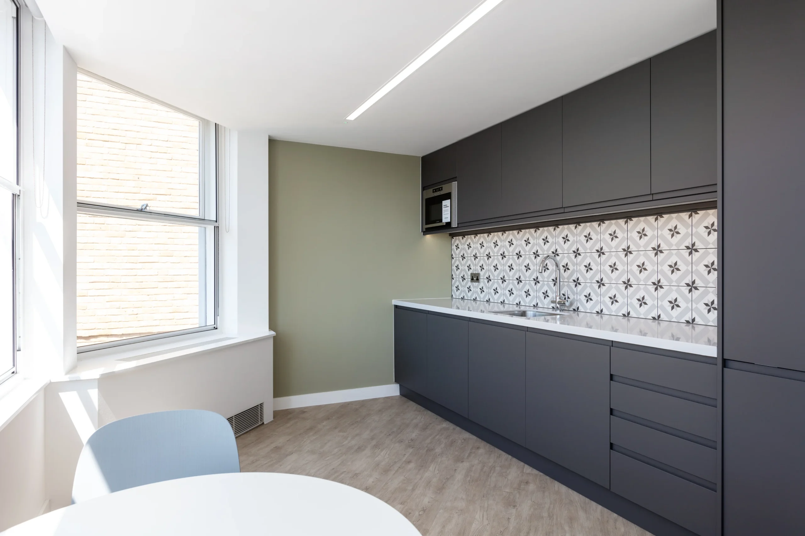 A small teapoint area with dark cabinetry and patterned backsplash tiles. The teapoint is equipped with a microwave and a round dining table.