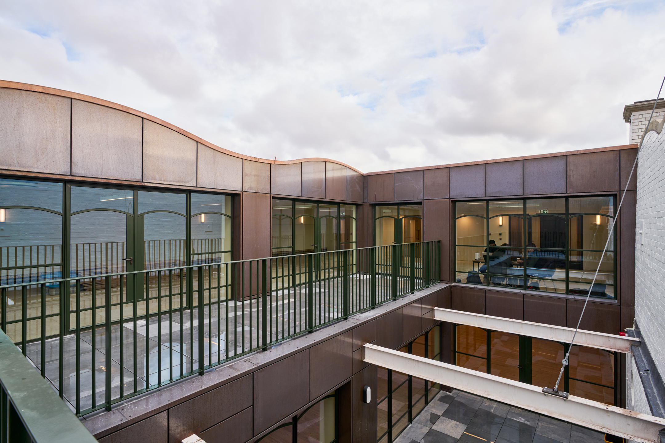 Second-floor outdoor terrace with metal railings and a curved roofline. The architecture blends glass and metal elements with large windows.