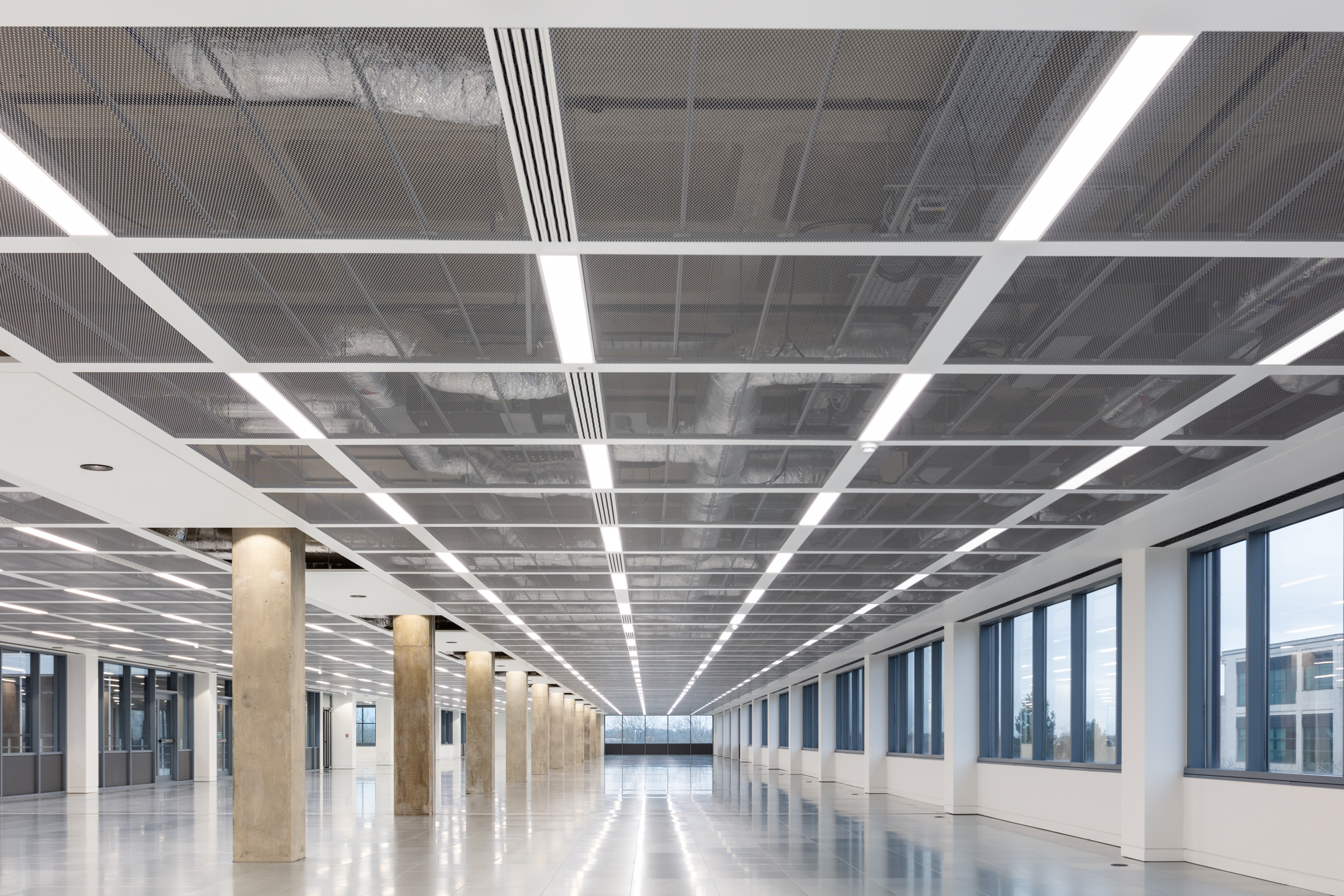 An open office floor with polished flooring and rows of ceiling lights at Witan Gate. The floor plan is spacious, with concrete pillars running along the room.