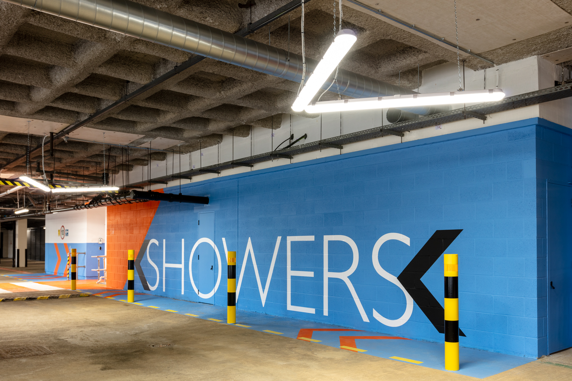 The shower area in the underground parking of Witan Gate. The space has colourful wall graphics and an industrial-style ceiling with exposed pipes.