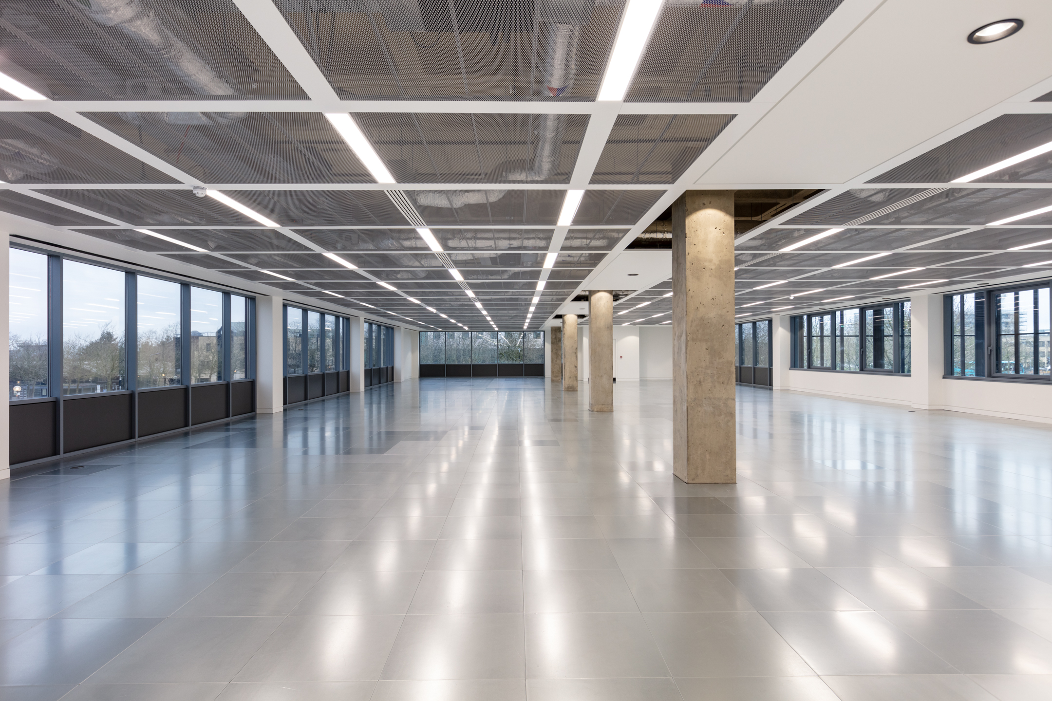 The open-plan office at Witan Gate, showcasing reflective flooring and ceiling panels that extend across the spacious interior. Multiple windows line the room, allowing natural light to fill the area.