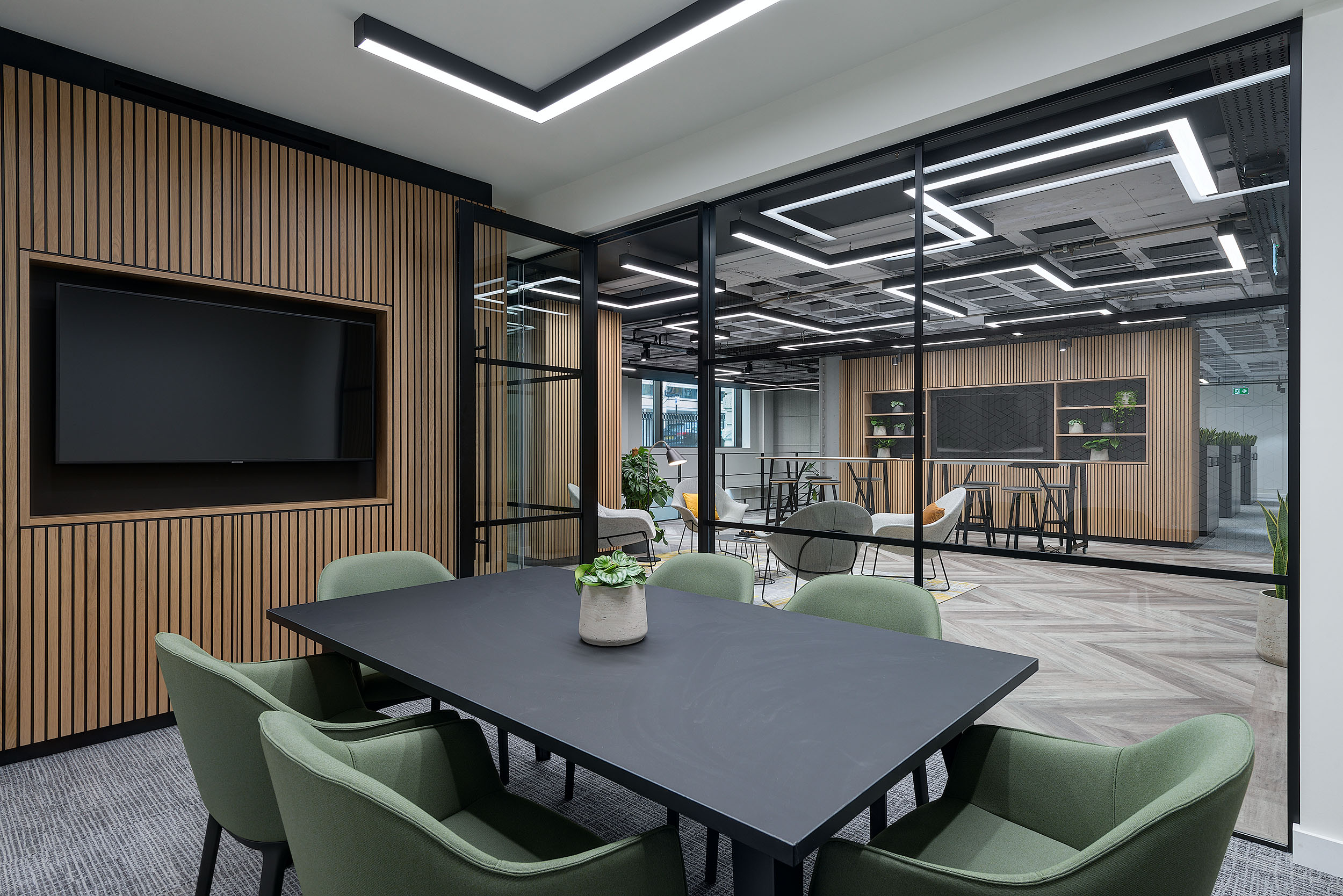 Oak and sage green meeting room. Green office chairs, oak wood panelling surronding screen with glass walls.