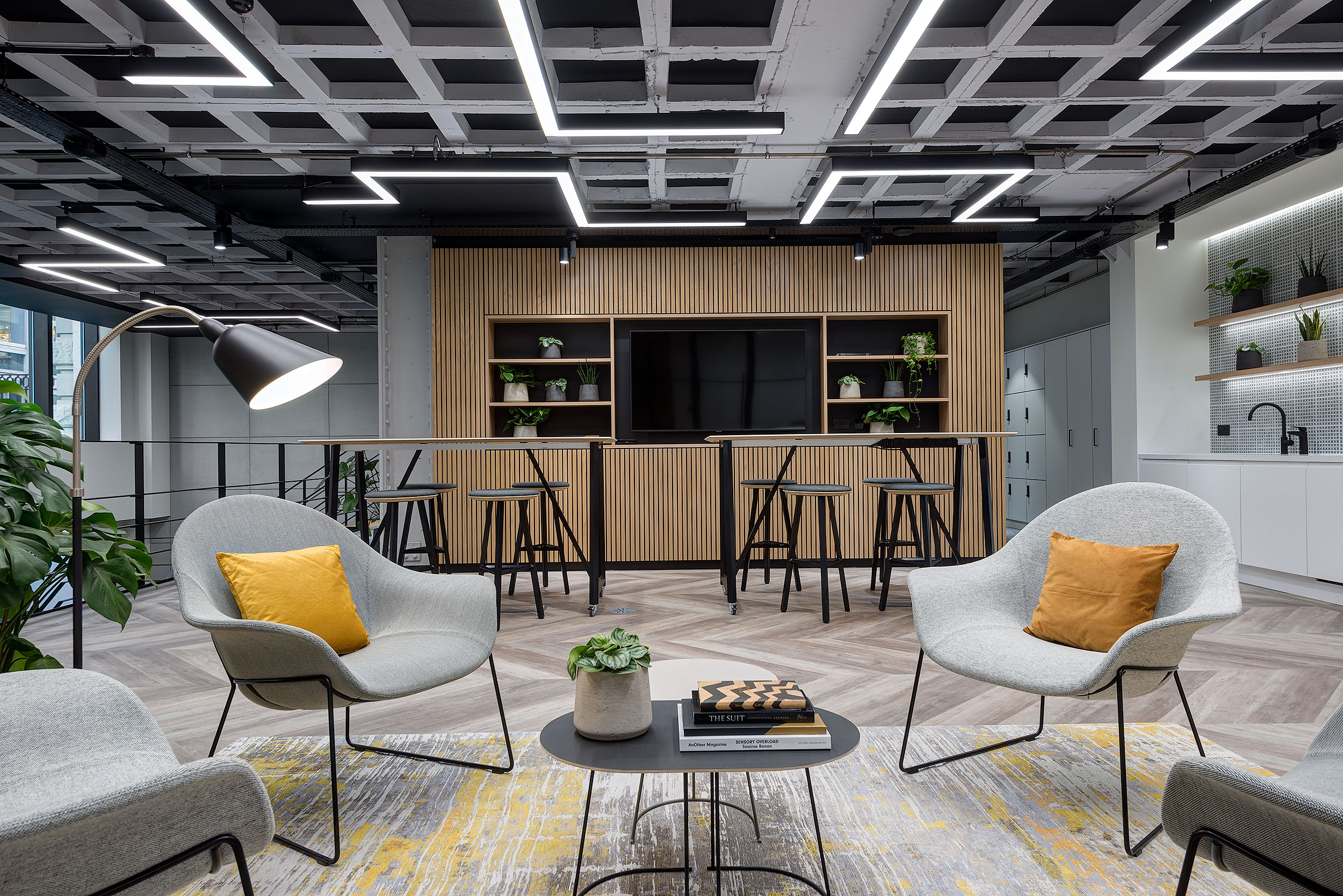 Large view of seating area with chairs, stools, and a black bookshelf for storage as the focus point.