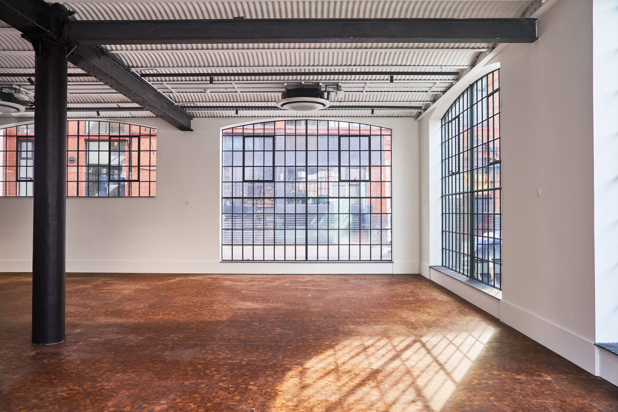 Open-plan interior of Voysey House with restored industrial-style windows, polished wooden flooring, and exposed steel beams under a ribbed ceiling.